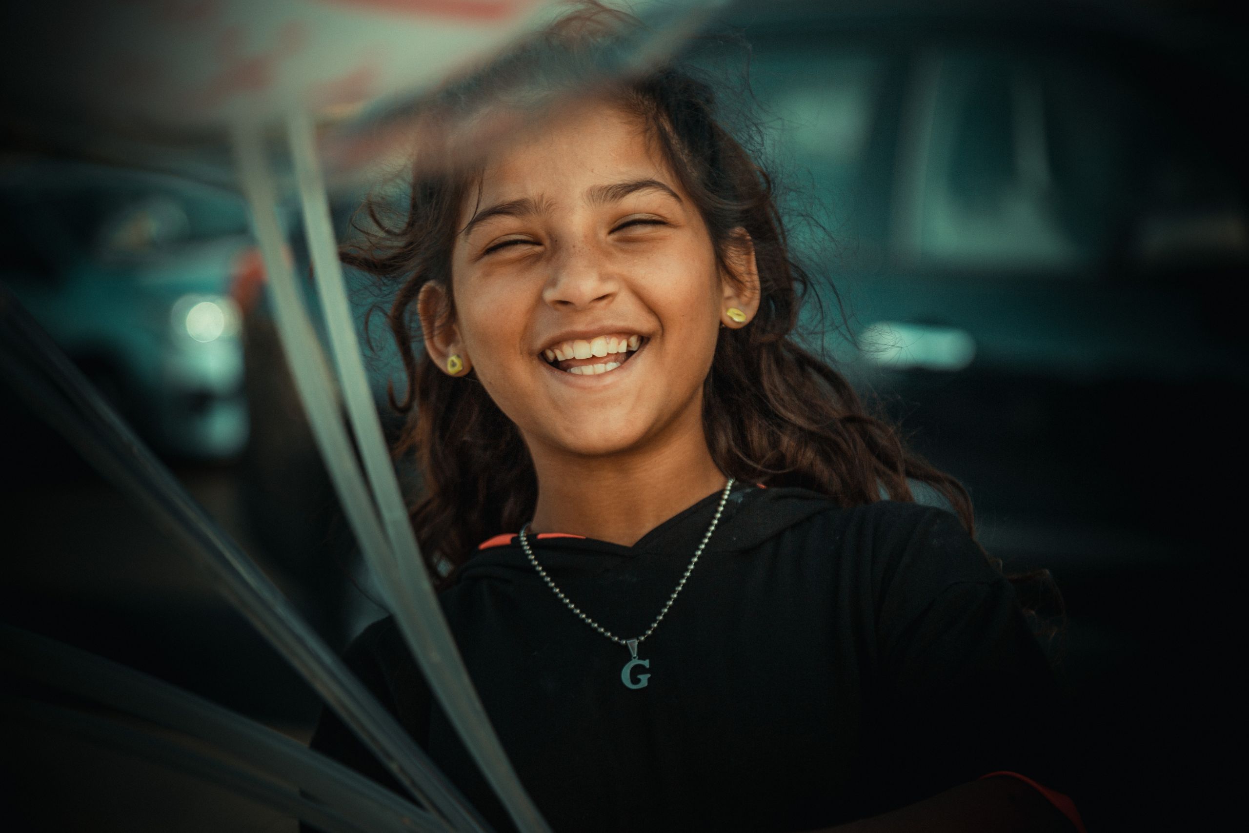 A newcomer youth smiling while in an outdoor setting near parked cars