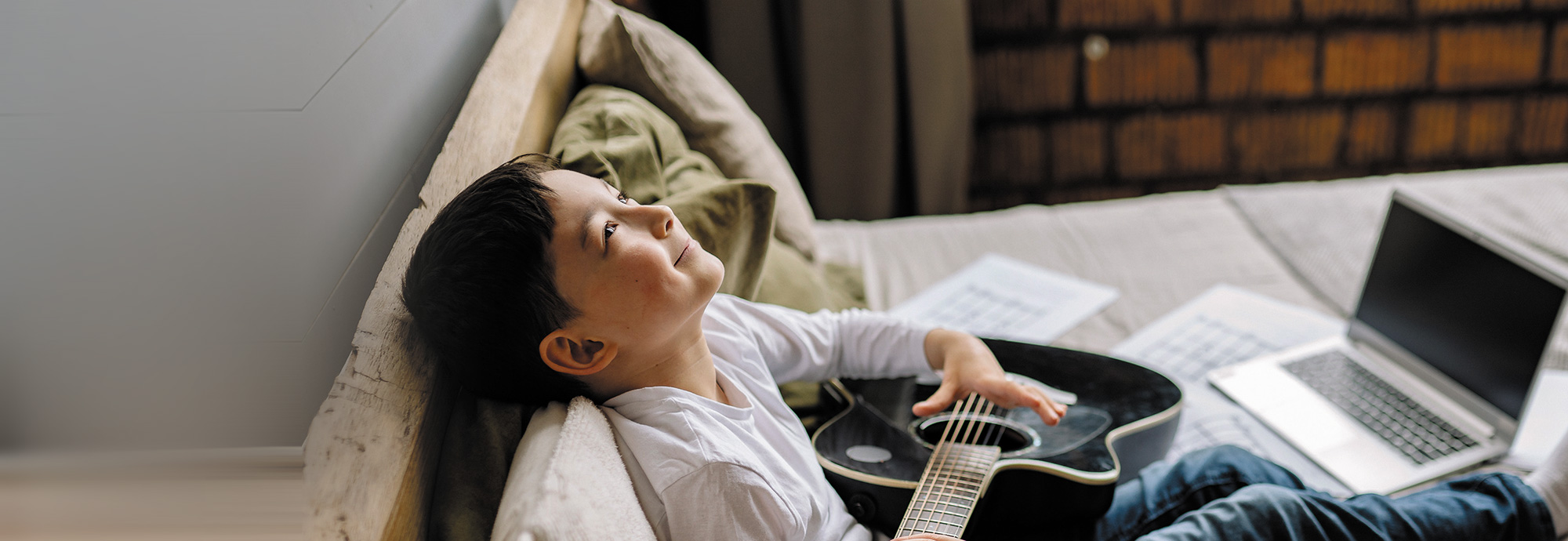 A young person holding a guitar and looking up at the ceiling