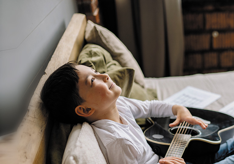 A young person holding a guitar and looking up at the ceiling