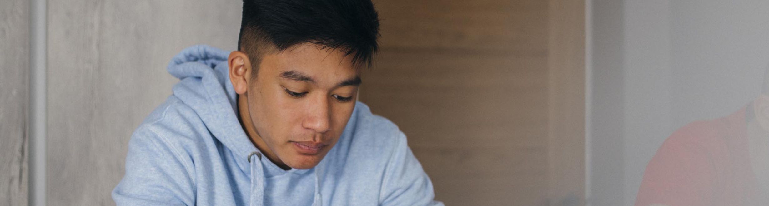 A young person sitting at a table while looking at a phone and reflecting on cyberbullying