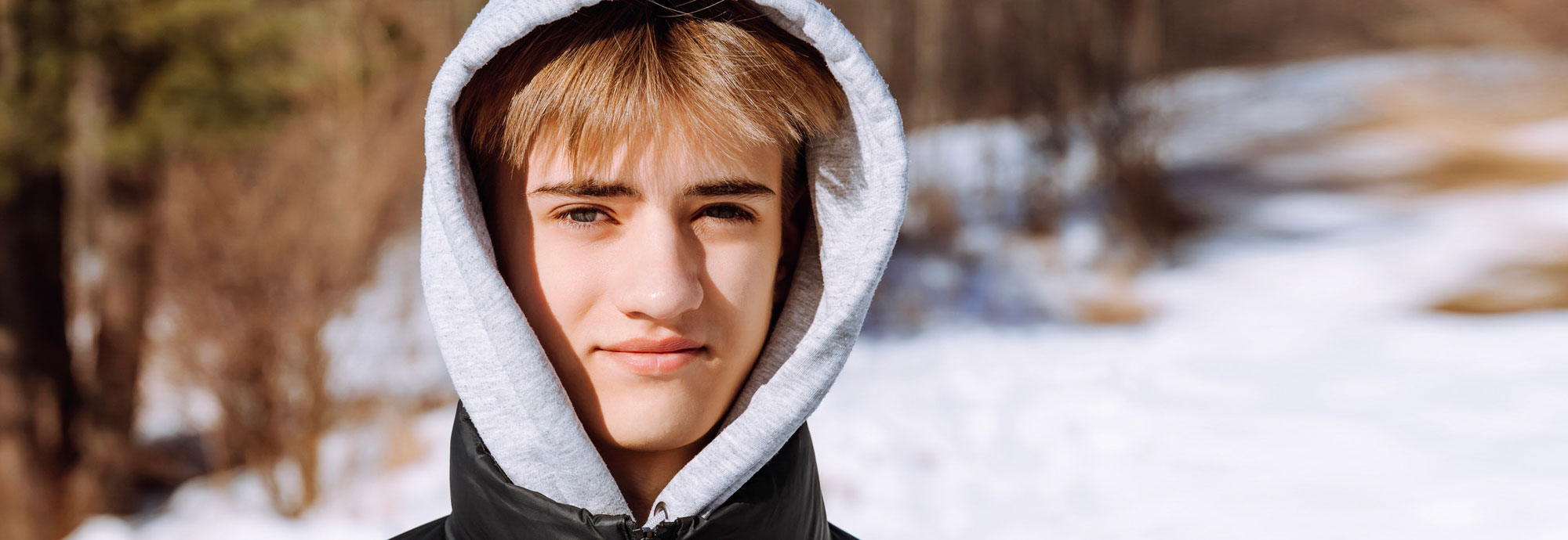 A young person standing outside in the snow, wearing a hoodie and looking directly into the camera