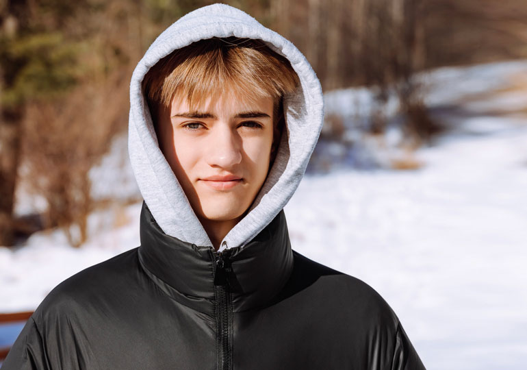 A young person standing outside in the snow, wearing a hoodie and looking directly into the camera