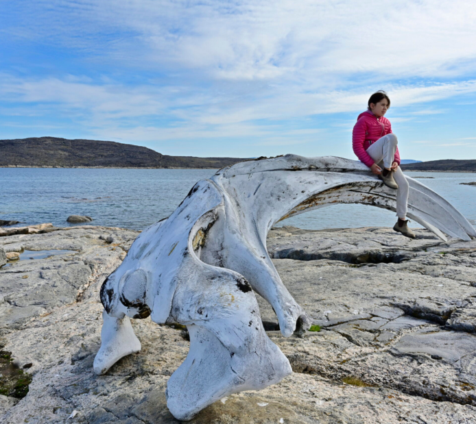 An Inuk young person perched on a whale bone along the Arctic shore of Baffin Island