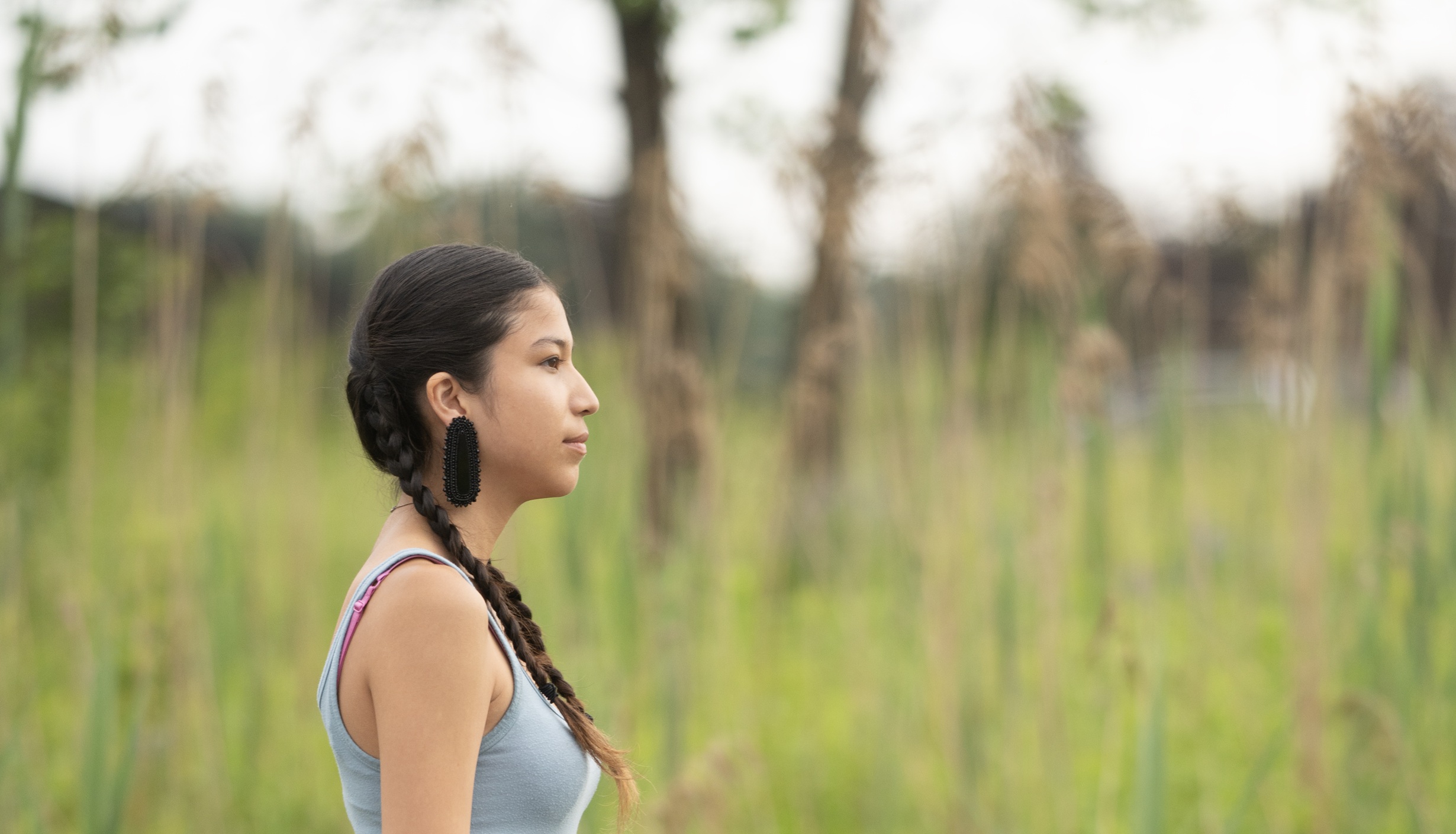 Young person walking on a road with tall grass behind them