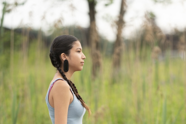 Young person walking on a road with tall grass behind them