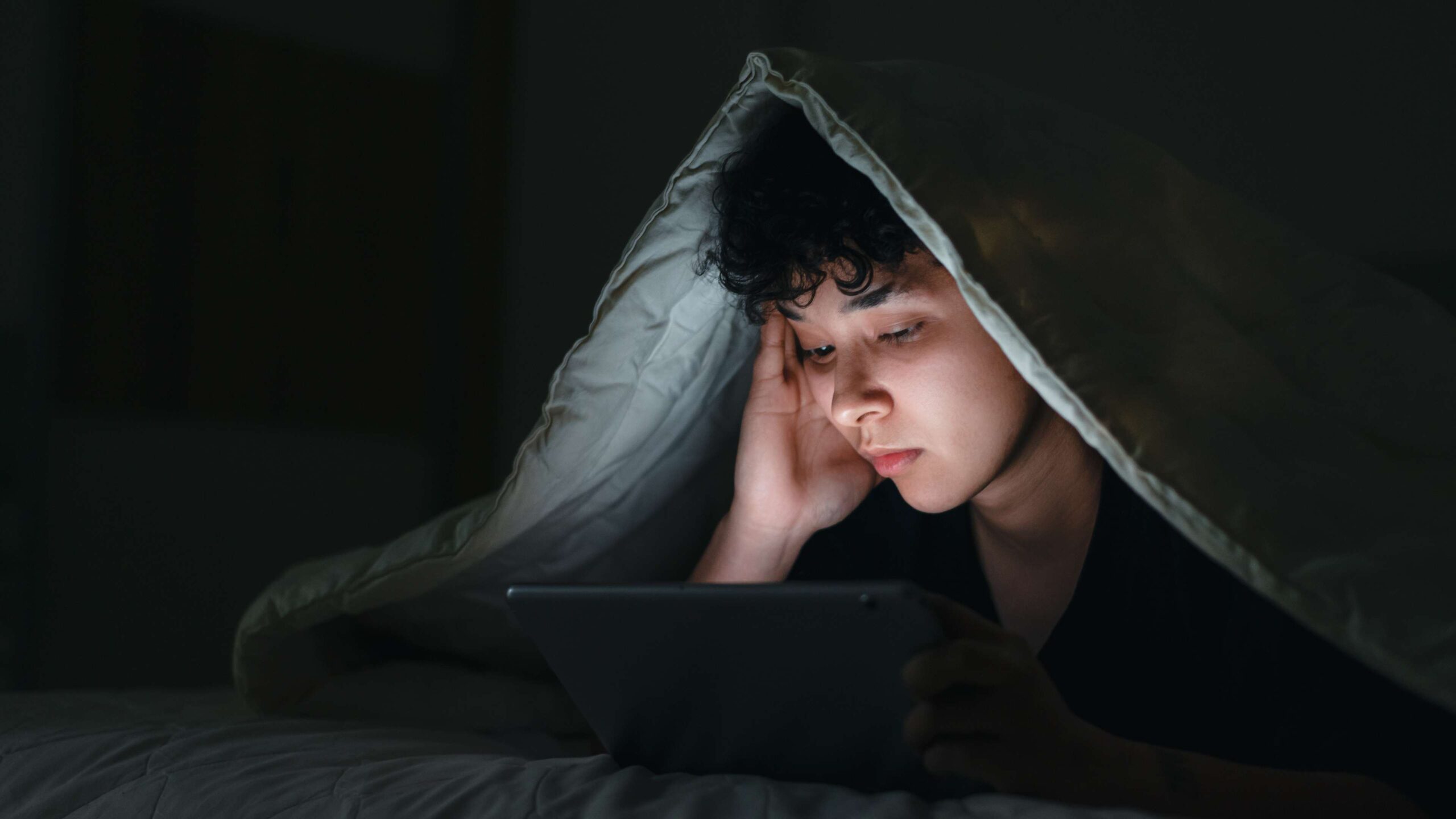 An image on a web page about Kids Help Phone’s mental health website of a young person hiding under a blanket looking at a tablet