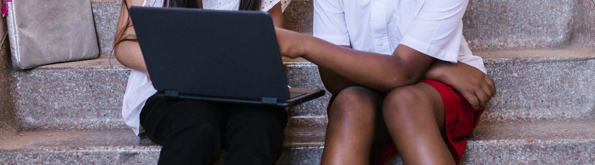 a boy and a girl looking at a laptop sitting on stairs