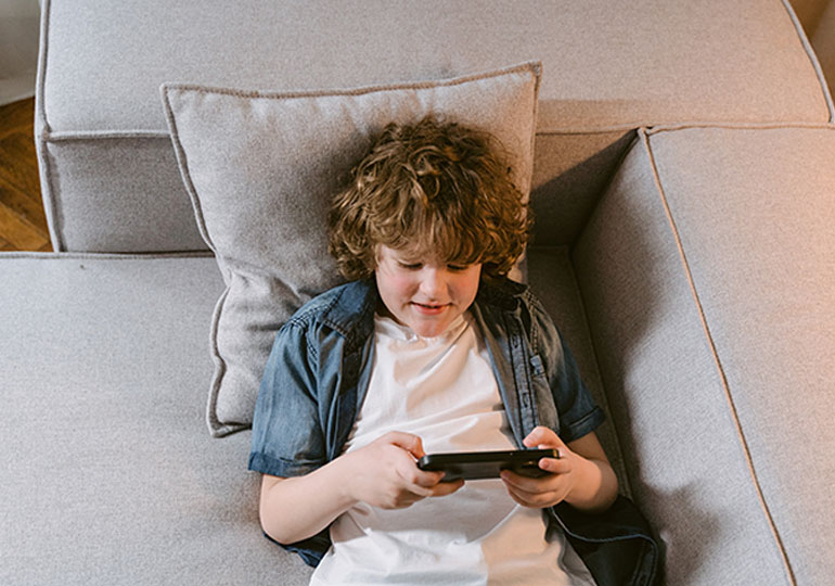 Young person lying on a couch while using a phone